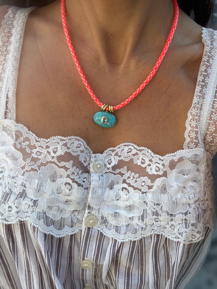 Woman wearing the Jordyn turquoise and aquamarine pendant on a orange paracord necklace with white lace top