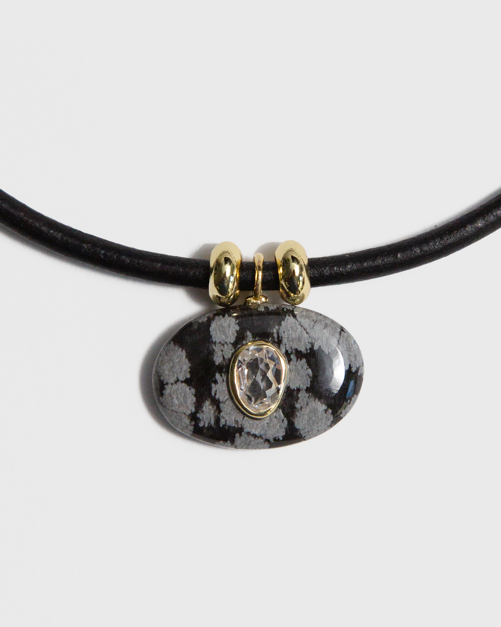 Necklace with a black cord and snowflake obsidian pendant on a light gray background