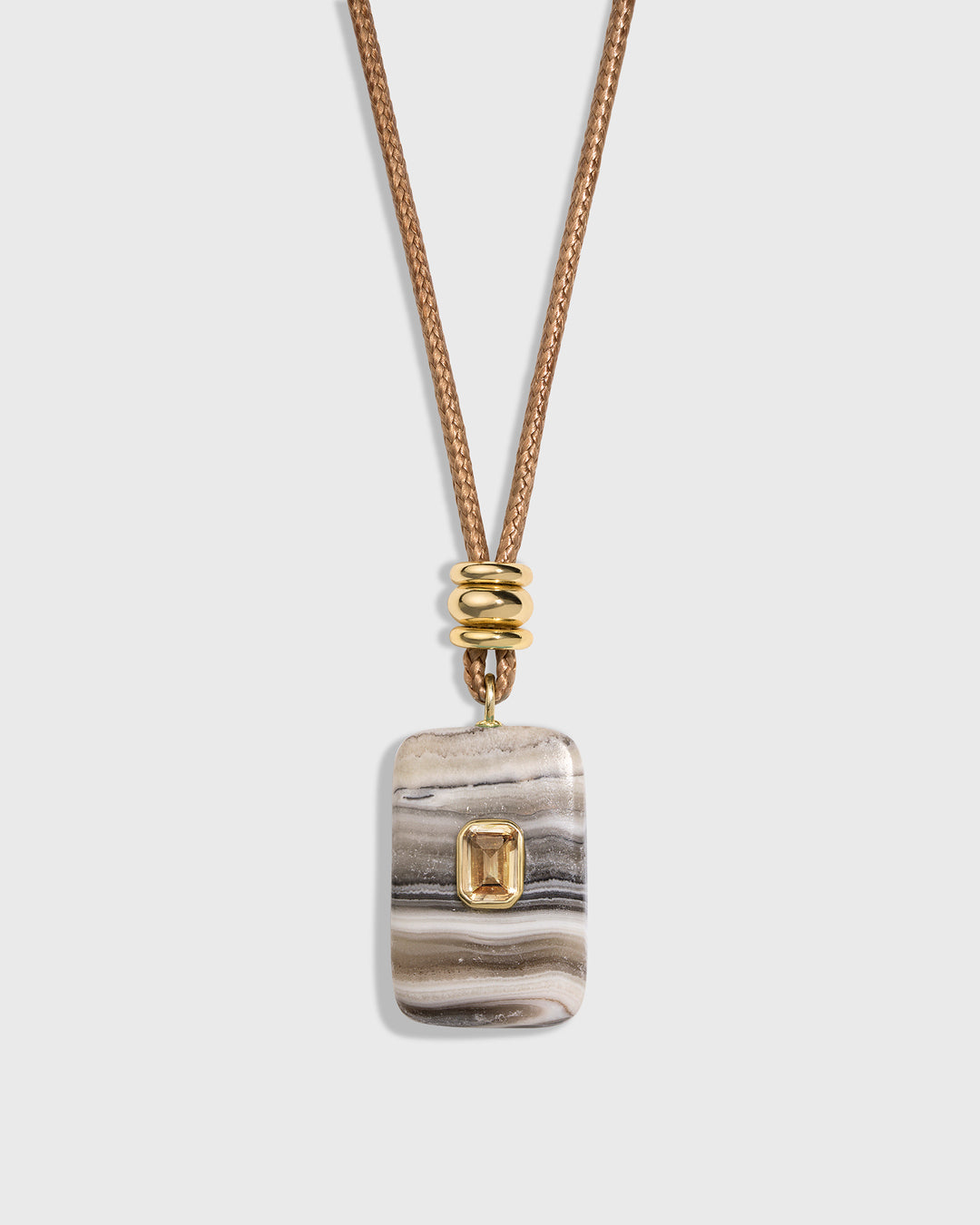 A rectangular stone pendant necklace with a gold bezel-set emerald-cut accent, hanging from a textured gold chain on a light gray background.