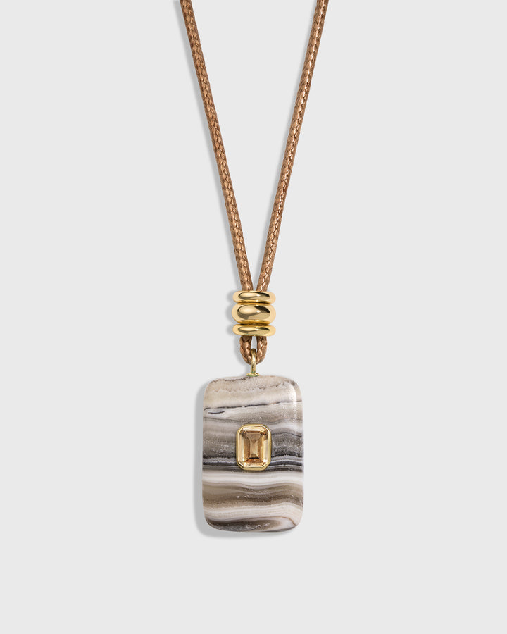 A rectangular stone pendant necklace with a gold bezel-set emerald-cut accent, hanging from a textured gold chain on a light gray background.