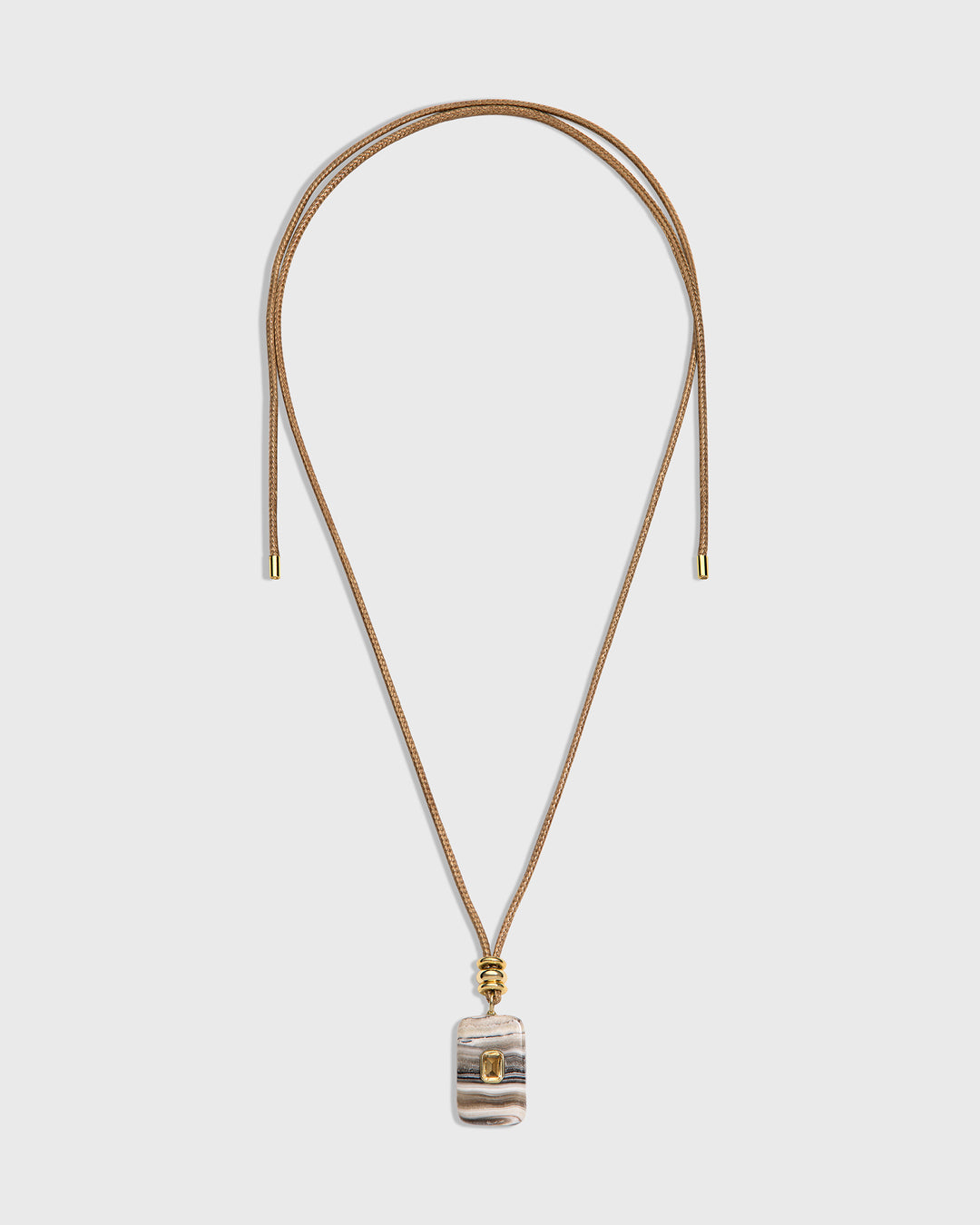 A long necklace with a thin tan cord and a small rectangular pendant featuring a striped pattern in beige, gray, and white, accented with gold-tone hardware.