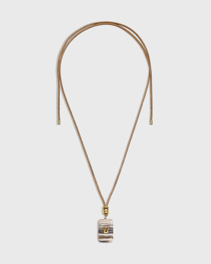 A long necklace with a thin tan cord and a small rectangular pendant featuring a striped pattern in beige, gray, and white, accented with gold-tone hardware.