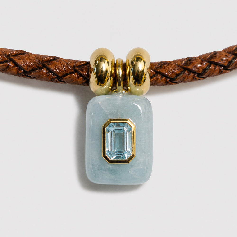 Jewelry with a aquamarine stone on a braided brown cord against a light grey background