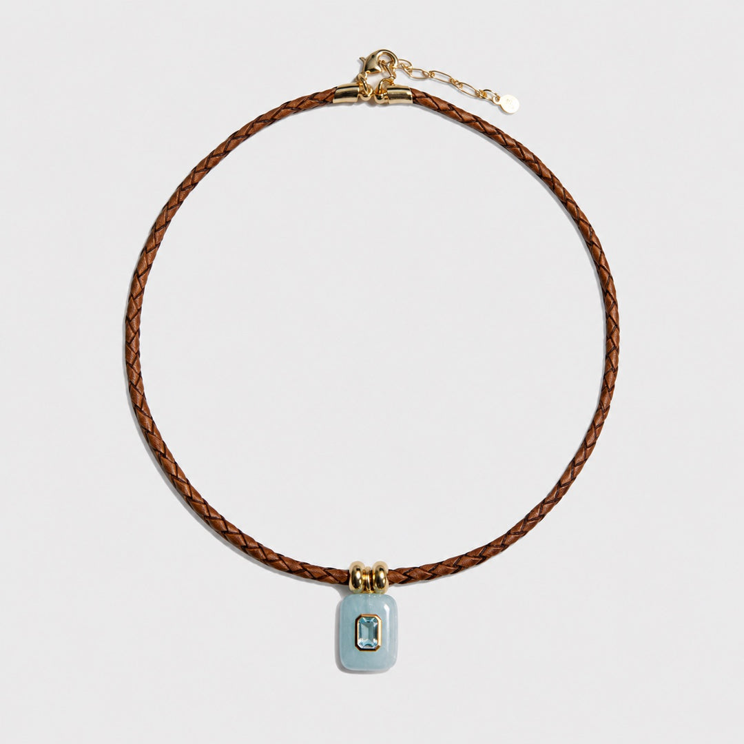 Necklace with brown leather cord and blue pendant on a light gray background