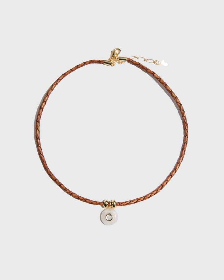 Brown braided leather necklace with a round pendant on a light gray background