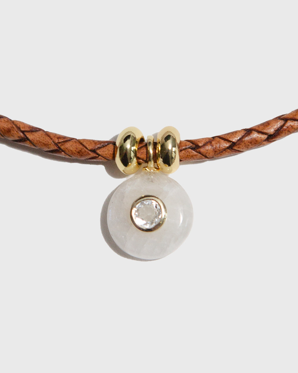 Bracelet with brown leather strap and gold and clear bead on a light grey background