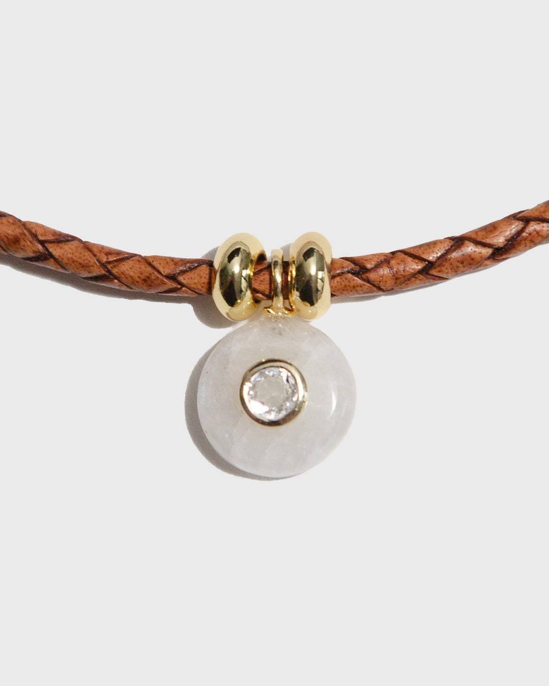 Bracelet with brown leather strap and gold and clear bead on a light grey background