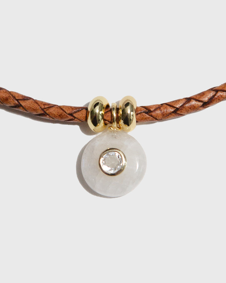 Bracelet with brown leather strap and gold and clear bead on a light grey background