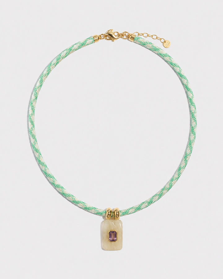 Necklace with green rope and gold clasp on a light grey background