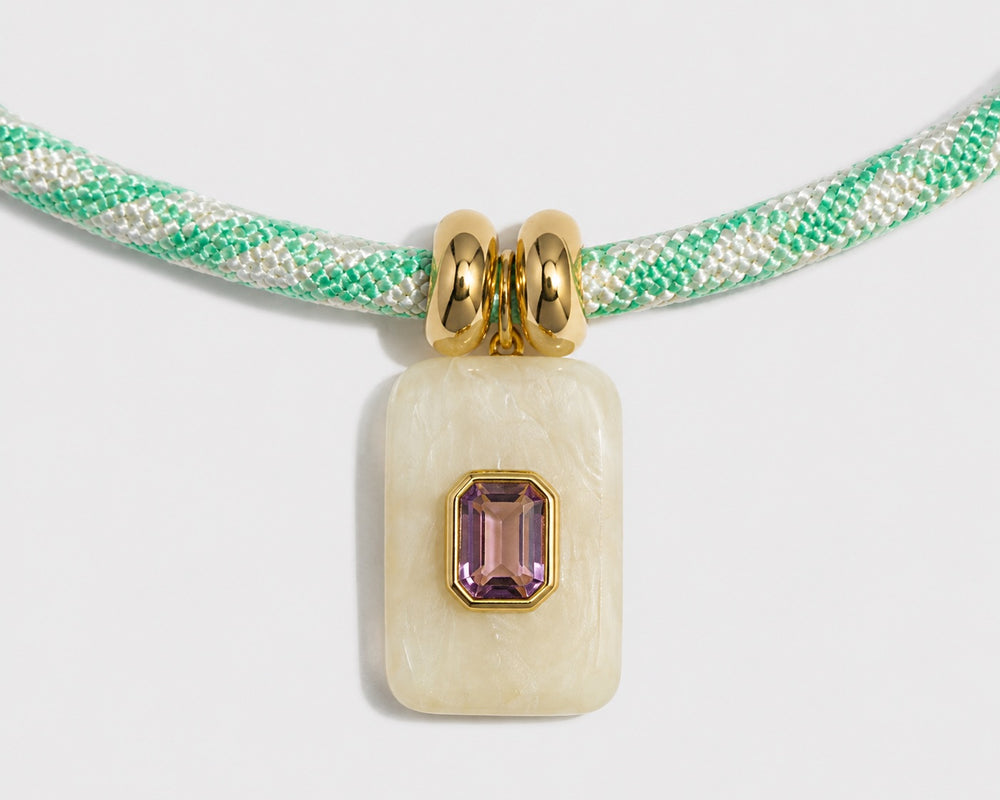 Necklace with a pendant featuring a green cord and gemstone on a light gray background