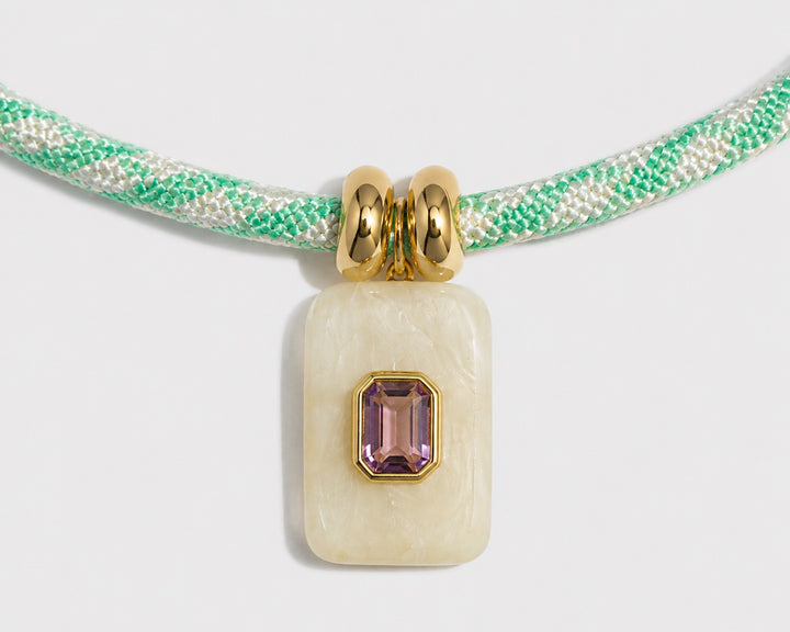 Necklace with a pendant featuring a green cord and gemstone on a light gray background