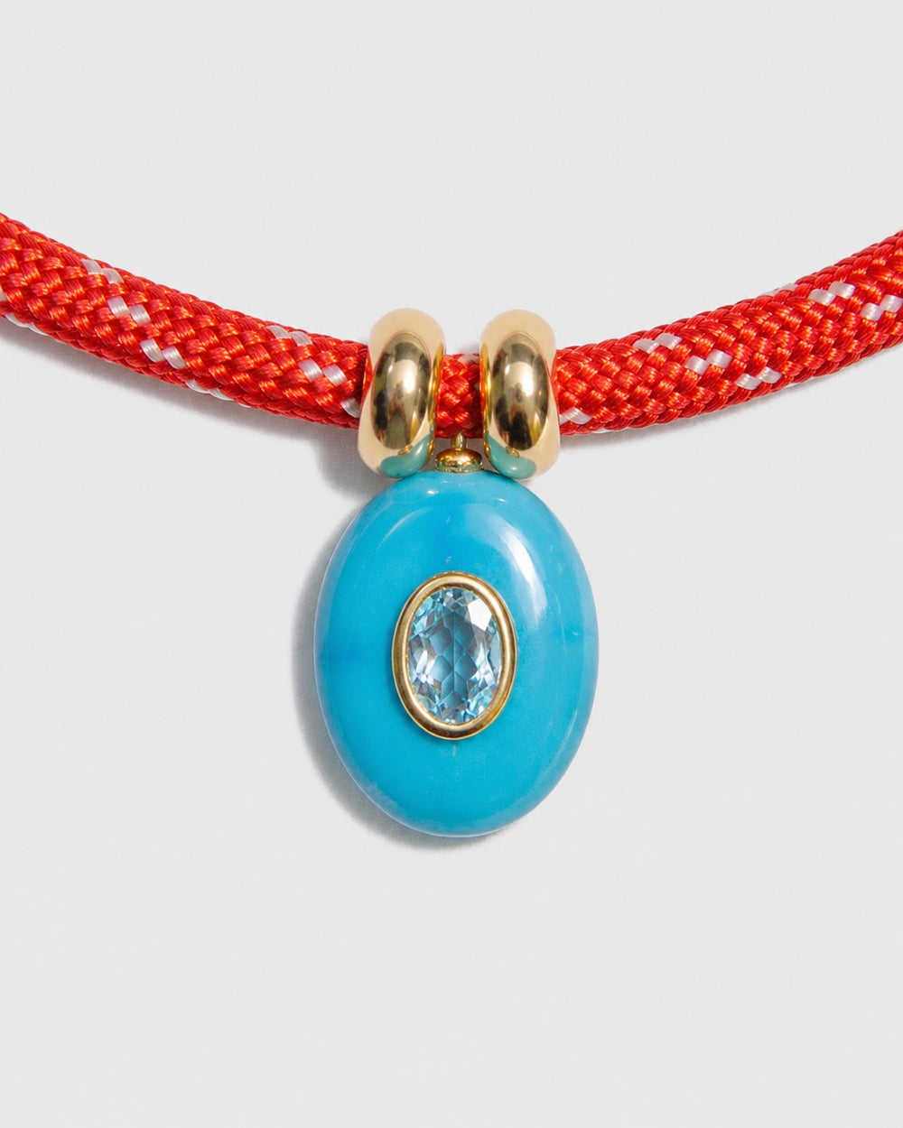 Turquoise pendant with gold accents on a red cord against a light gray background