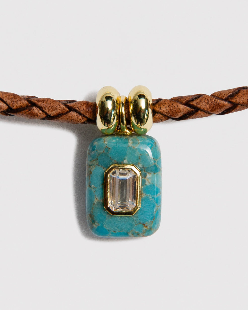 Turquoise pendant with gold accents on a braided brown cord against a light gray background